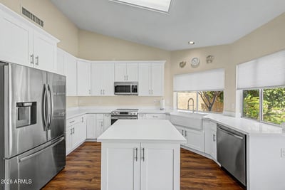 White cabinetry, a farmhouse-style sink, stainless steel appliances, and generous counter space highlight this impressive kitchen. The center island provides additional prep space and gathering room for guests.