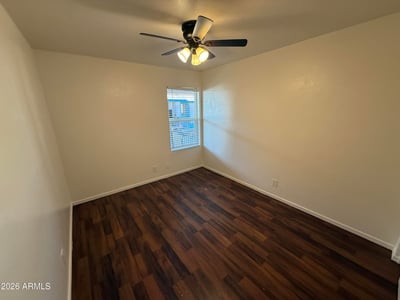 Comfortable bedroom featuring wood-look flooring, ceiling fan, and natural light. The spacious layout provides a relaxing retreat while accommodating a variety of furniture configurations.