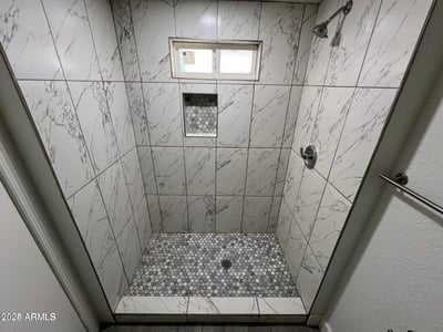 This impressive walk-in shower highlights oversized marble-look tile, a built-in niche for convenience, and stylish finishes throughout. The updated design creates a luxurious feel within this remodeled Phoenix residence.
