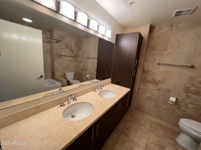 Primary bathroom featuring dual sinks, extensive counter space, contemporary cabinetry, and elegant stone finishes. A thoughtfully designed space offering comfort, storage, and everyday convenience.