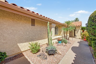 The private courtyard entrance showcases beautiful desert landscaping, mature palms, decorative stonework, and a tranquil covered walkway that welcomes guests with style.