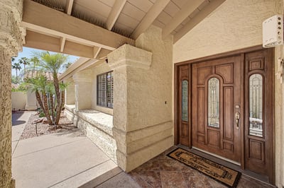 Elegant custom double entry doors create a warm and sophisticated welcome beneath a covered front patio. The gated entry enhances privacy while adding architectural character.