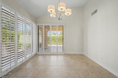 Light-filled dining room with stylish chandelier, plantation shutters, and courtyard access creates an inviting setting for everyday meals and entertaining guests.