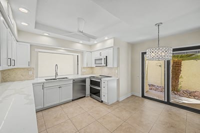 Open kitchen and dining area featuring quartz countertops, white shaker cabinets, stainless steel appliances, designer lighting, and direct access to the private courtyard for seamless indoor-outdoor living.
