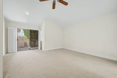 Spacious owner's suite with vaulted ceilings, plush carpet, plantation shutters, and sliding glass doors providing natural light and easy access to the private outdoor patio.