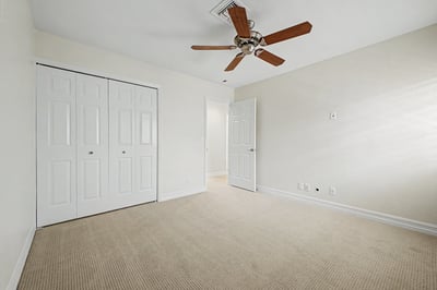 Spacious bedroom with generous closet storage, ceiling fan, plush carpeting, and neutral d cor, offering flexible living space for guests, hobbies, or remote work.