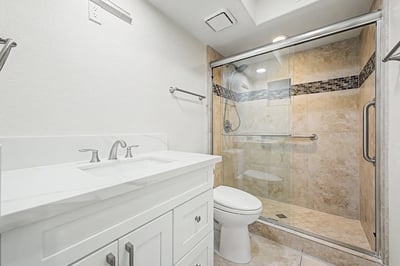 Updated bathroom showcasing a quartz vanity, elegant tiled walk-in shower, glass enclosure, and contemporary fixtures for everyday comfort and convenience.