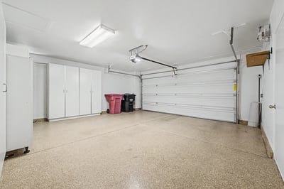 Clean, oversized garage with built-in cabinetry, epoxy-coated flooring, and organized storage solutions, offering functionality beyond vehicle parking.