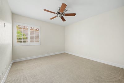 Bright guest bedroom featuring plantation shutters, plush carpeting, ceiling fan, and neutral finishes that easily accommodate family, visitors, or a home office.