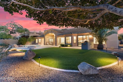 Beautiful evening exterior highlighting the pool, covered patio, outdoor seating, lush landscaping, and custom BBQ area. This Scottsdale property is ideal for entertaining day or night.