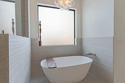 Elegant soaking tub surrounded by designer tile, oversized window, and modern lighting. A peaceful retreat designed for comfort and relaxation within the luxurious primary suite.