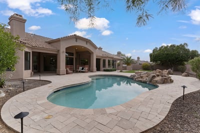 Beautiful outdoor living space featuring a sparkling swimming pool, expansive paver patio, artificial turf, mature landscaping, and generous entertaining areas in this Scottsdale home.