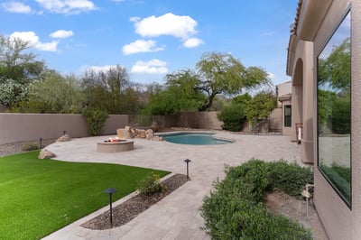 Private Scottsdale backyard featuring a sparkling swimming pool, custom fire pit, expansive paver patio, artificial turf, and mature landscaping designed for relaxing and entertaining.