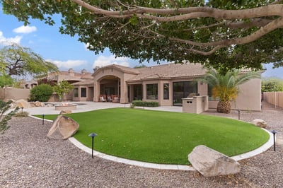 Resort-inspired backyard with a covered patio, sparkling pool, outdoor kitchen, artificial lawn, and generous entertaining space. A beautiful extension of this Scottsdale home's luxury living.