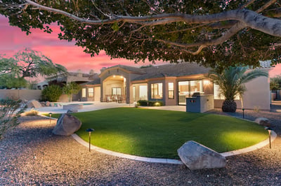 Beautiful evening exterior highlighting the pool, covered patio, outdoor seating, lush landscaping, and custom BBQ area. This Scottsdale property is ideal for entertaining day or night.