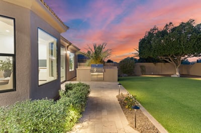 Custom outdoor kitchen with built-in grill surrounded by elegant paver walkways, artificial turf, and landscape lighting. A perfect Scottsdale backyard for hosting family and friends.