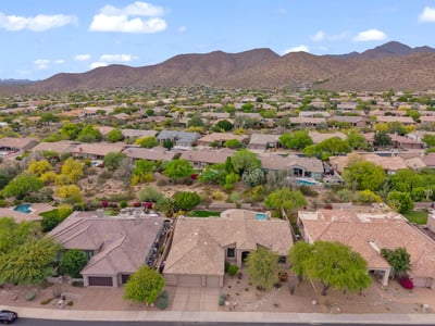 Sweeping aerial perspective capturing the Scottsdale neighborhood, nearby mountain scenery, mature desert landscaping, and the home's desirable residential setting.