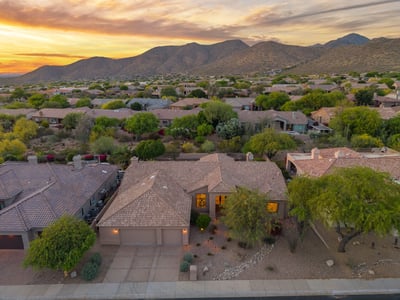 Beautiful sunset aerial featuring the home's attractive exterior framed by breathtaking mountain views and mature desert landscaping. This Scottsdale residence offers an exceptional setting with outstanding curb appeal.