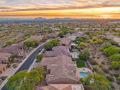 Expansive aerial capturing the surrounding Scottsdale neighborhood, dramatic mountain scenery, nearby desert wash, and the home's desirable location among beautifully maintained luxury residences.