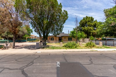 A full view of the property showcases the oversized lot, mature landscaping, covered parking, and generous front yard. Buyers will appreciate the outdoor space, curb appeal, and convenient Mesa location.