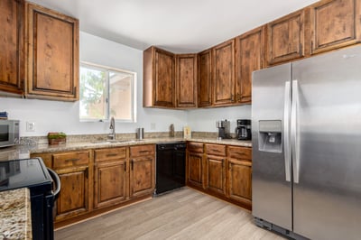 This angle emphasizes the kitchen's abundant cabinetry, granite countertops, stainless steel refrigerator, and efficient workspace. Updated finishes create a warm and inviting heart of the home.