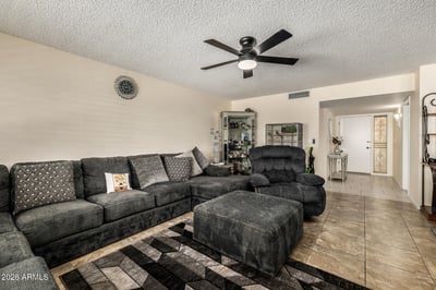 Comfortable family room featuring large windows with plantation shutters, tile flooring throughout, modern ceiling fan, and a spacious layout ideal for everyday living and entertaining.