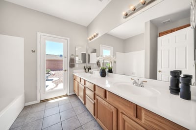 Spacious bathroom with an extended dual-sink vanity, ample cabinet storage, and exterior access to the backyard. Perfect for guests returning from the pool or everyday convenience.