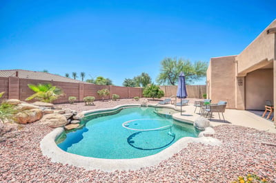 Beautiful backyard showcasing a PebbleTec pool, cascading rock waterfall, and spacious patio surrounded by desert landscaping. A peaceful outdoor oasis designed for entertaining and everyday enjoyment in Goodyear.