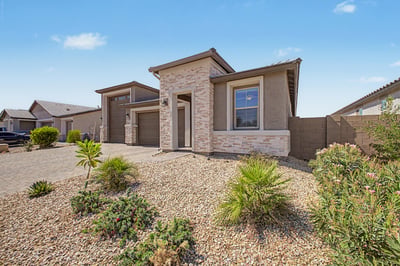 Covered front entry framed by elegant stonework welcomes guests with timeless style. Desert landscaping and quality exterior finishes create lasting curb appeal.