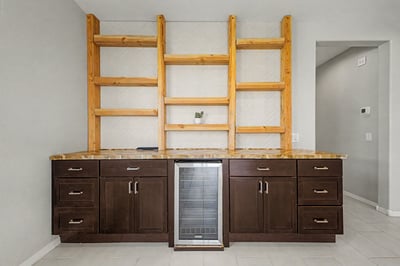 Custom cabinetry with rich wood shelving and integrated beverage refrigerator provides elegant storage and display space, making this bonus area both beautiful and functional.