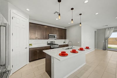 Bright kitchen with expansive quartz island, stainless steel appliances, pendant lighting, and open sightlines to the living area. The spacious layout is ideal for hosting guests or everyday family living.