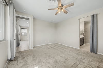 Generously sized primary bedroom with soft carpeting, neutral tones, ceiling fan, and convenient access to the walk-in closet and ensuite bath. A peaceful space to begin and end each day.