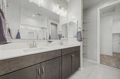 Spacious primary bathroom with dual quartz vanities, contemporary lighting, oversized mirrors, built-in storage shelves, and convenient access to the walk-in closet. Blending elegance with everyday functionality.