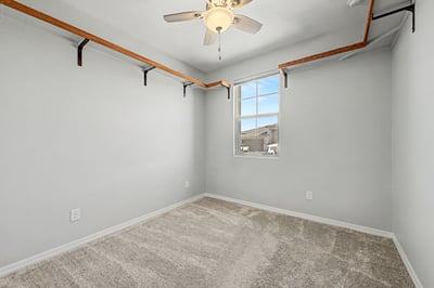 Bright secondary bedroom with plush carpeting, ceiling fan, custom open shelving, and a large window. Perfect as a guest room, home office, or hobby space in this beautiful Wittman residence.