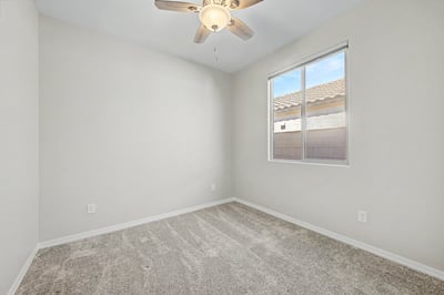 Secondary bedroom with plush carpet, ceiling fan, and abundant natural light. The clean, neutral design provides a move-in-ready space suitable for guests or everyday living.