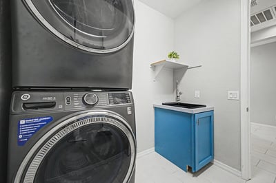 Dedicated laundry room equipped with a utility sink, storage cabinet, shelving, and stacked washer and dryer. A practical feature that simplifies everyday household routines.