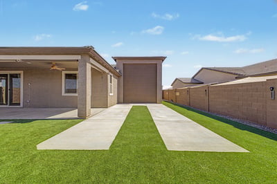 Rear yard view highlighting the dedicated RV garage, covered patio, manicured artificial turf, and thoughtfully designed outdoor spaces that complement this exceptional Wittman home.