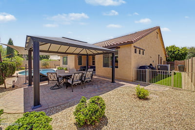 Another view showcases the spacious covered patio, attractive paver surfaces, and beautifully maintained backyard that complements the private pool in this Goodyear rental home.
