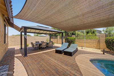 This spacious backyard combines a covered dining pavilion, shade canopy, poolside lounge chairs, and paver patio to create an exceptional outdoor entertaining area in Goodyear.