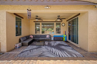 Enjoy year-round outdoor comfort beneath the covered patio complete with ceiling fans, comfortable seating, sliding glass door access, and views of the beautifully landscaped backyard in Goodyear.