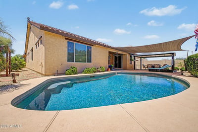 Enjoy resort-style outdoor living with a sparkling pool, covered entertaining area, shade sail, paver patio, and low-maintenance landscaping that make this Goodyear rental ideal for relaxing year-round.