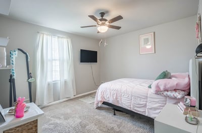 Spacious bedroom featuring a ceiling fan, plush carpeting, and natural light from large windows.
