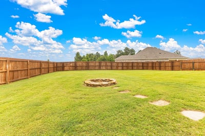 Spacious backyard featuring a stone fire pit and a privacy fence, perfect for outdoor gatherings.