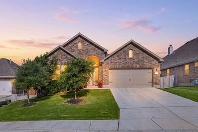 This modern brick home features a spacious driveway, lush landscaping, and stunning sunset views.