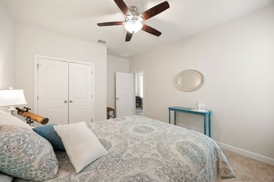 Spacious bedroom featuring a ceiling fan, natural light, and a functional layout with ample storage options.