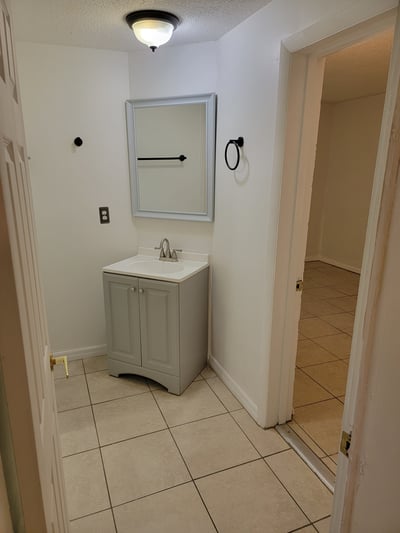 Bright bathroom featuring a modern vanity and ample tile space, leading into an additional room beyond.