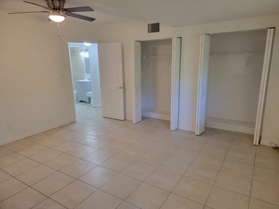 Spacious bedroom featuring tile flooring, dual closets, and an adjoining bath for convenient living.