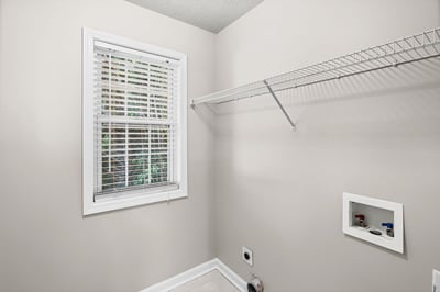 Bright and functional laundry room featuring ample shelving and natural light through the window.