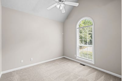 Bright and airy room featuring a large arched window and plush carpeting, perfect for personalized décor.