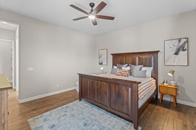 Spacious bedroom featuring warm wood tones, modern furnishings, and a ceiling fan for added comfort.